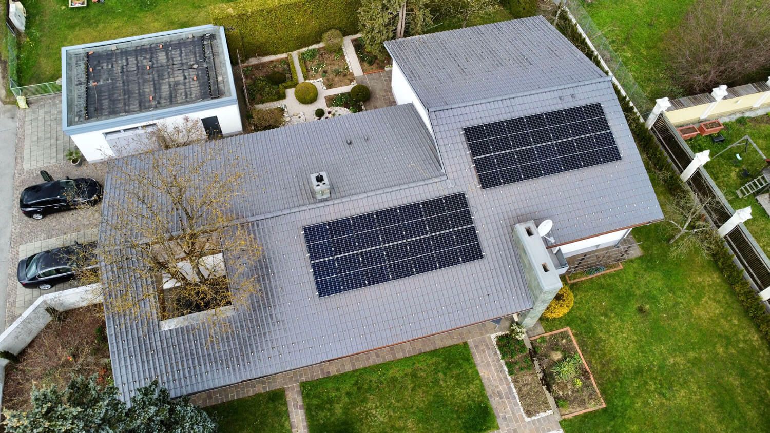 Luftaufnahme eines Hauses mit grauem Dach und zwei Modulfeldern, daneben Garten und Stellplätze.