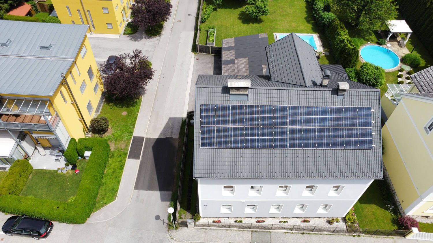 Mehrparteienhaus mit grauem Dach und durchgehendem Modulfeld, links ein gelbes Nachbargebäude.