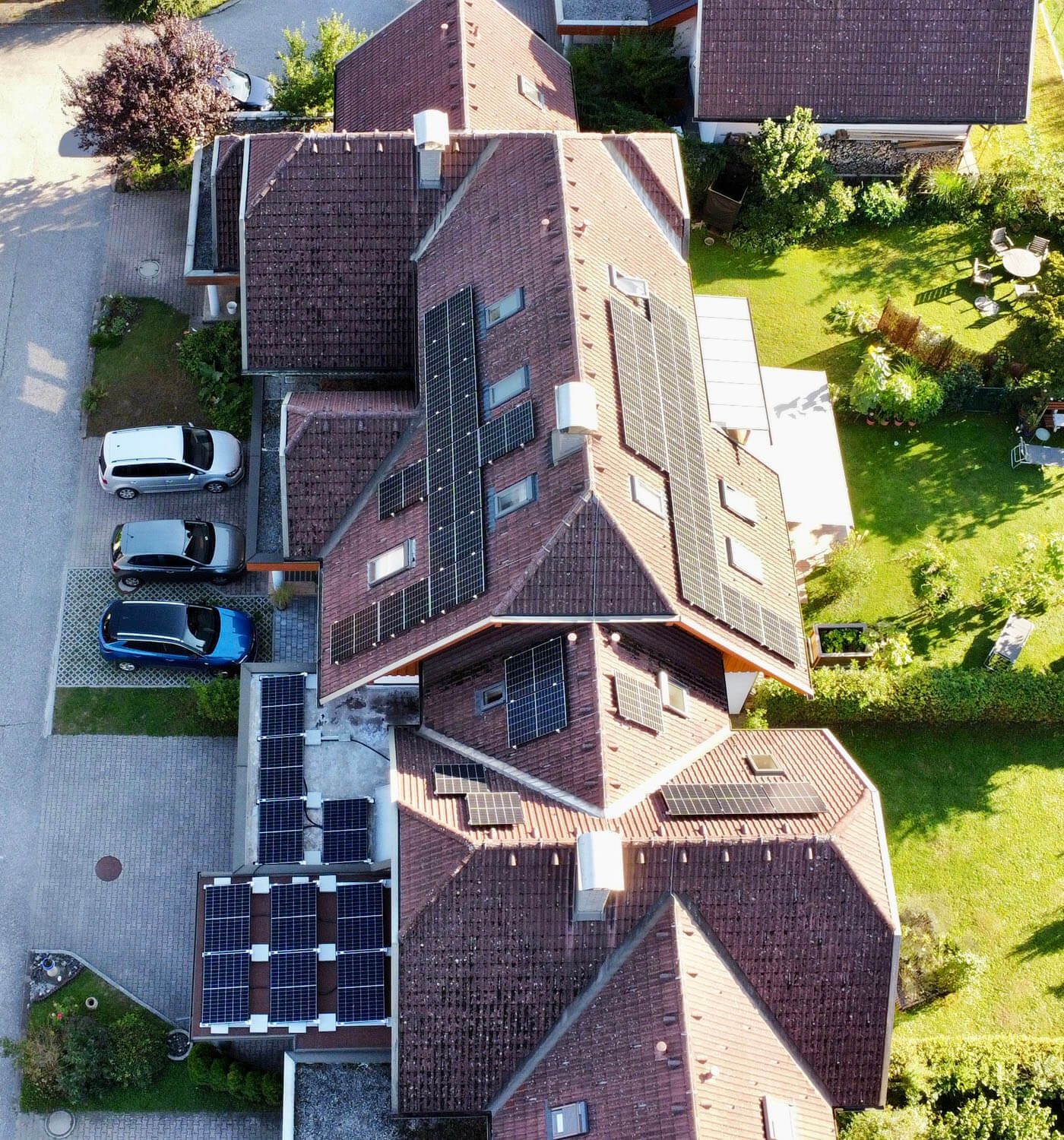 Senkrechte Luftaufnahme mehrerer aneinandergebauter Häuser mit braunen Ziegeldächern und Modulreihen auf mehreren Dachflächen.